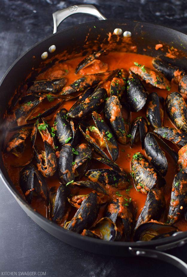 Mussels in spicy red arrabbiata sauce in a lidded pan with cream and freshly chopped parsley over the top