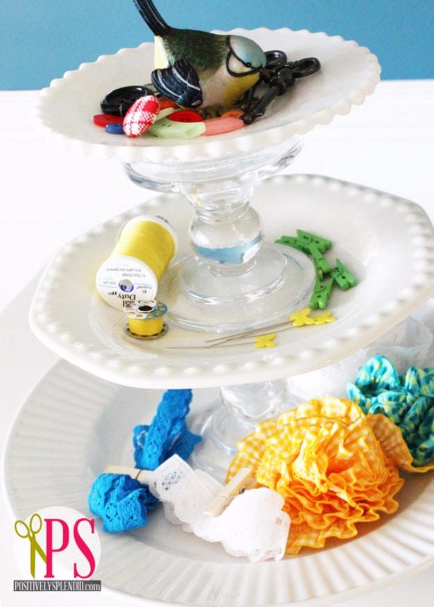 White tiered cake stand beside a sewing machine holding thread, buttons, snips, trim and other notions