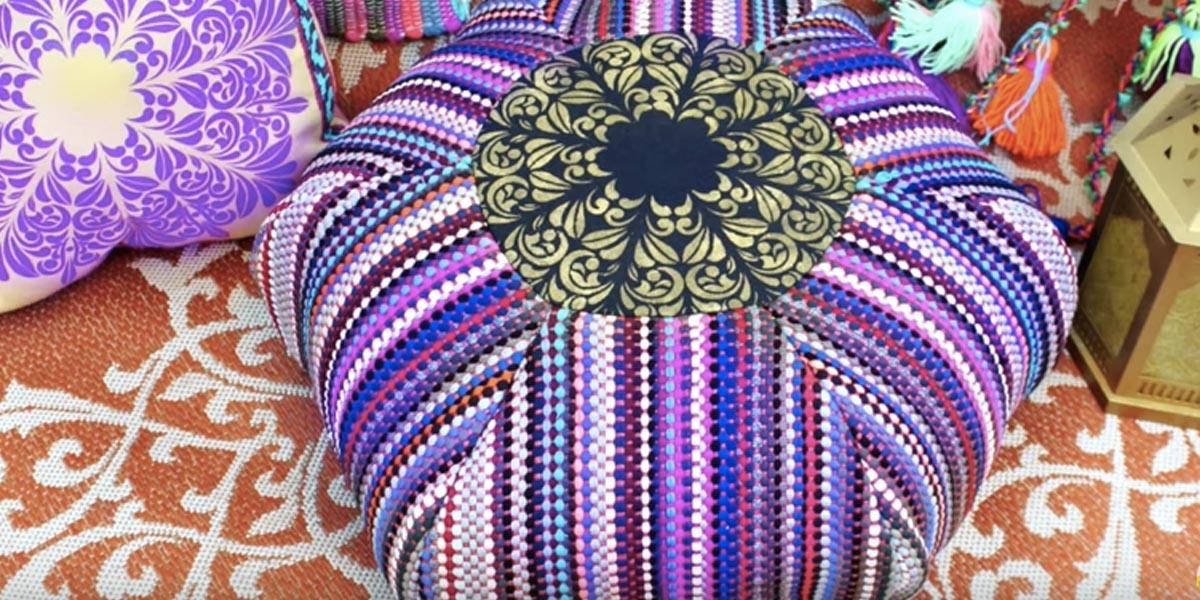 Round boho rag rug floor pouf in purple and blue stripes with a gold medallion center, on an orange patterned rug