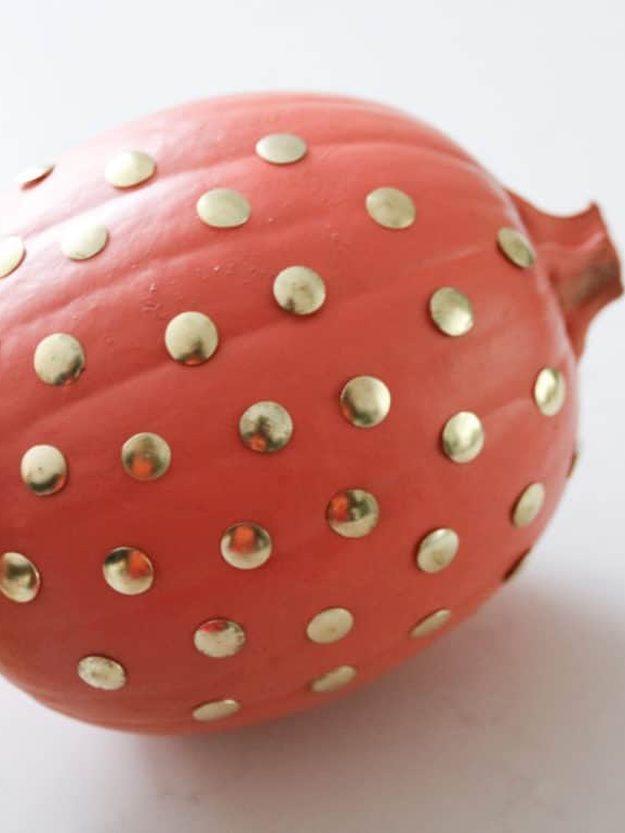 Coral painted pumpkin covered all over in evenly spaced brass gold thumbtacks pressed flush into the skin