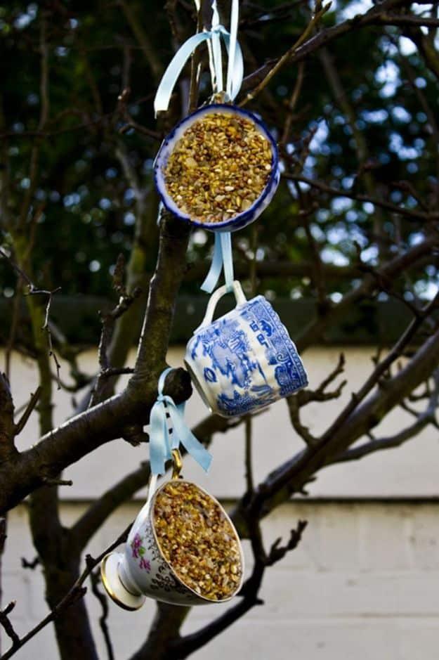 Three vintage teacups and a saucer packed with seed and fat, blue willow and floral china hung in a bare tree