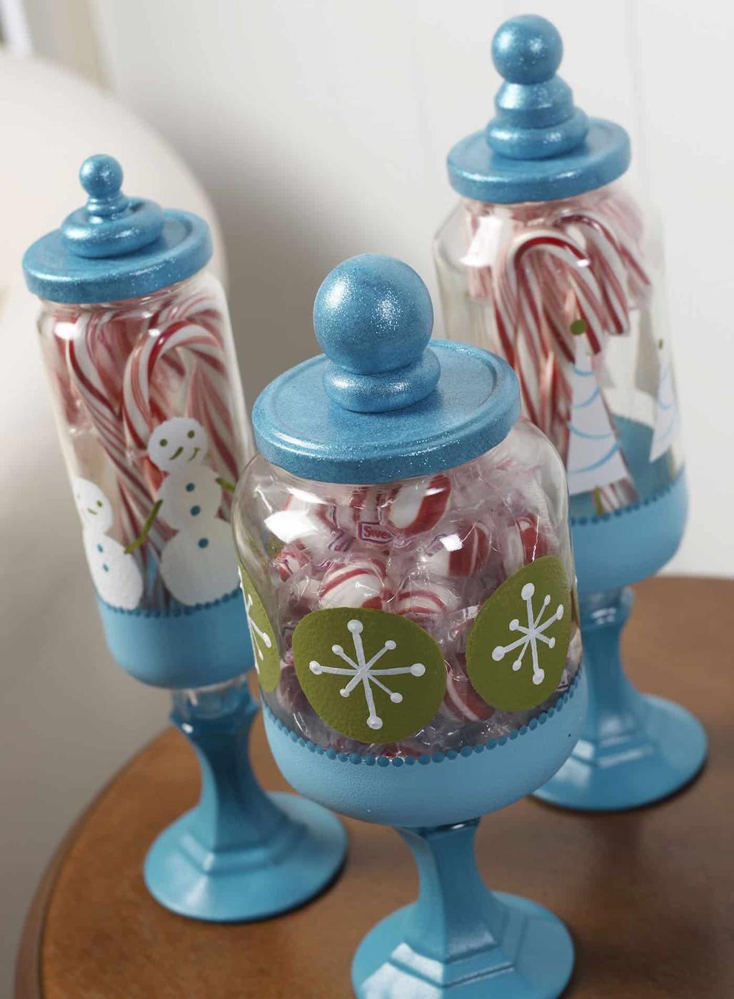 Three glass apothecary jars with pedestal bases and lids filled with red and white holiday candy on a mantel