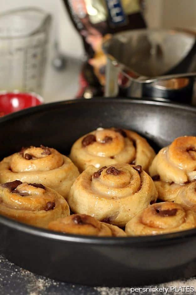 Chocolate chip cinnamon rolls made from crescent dough in a round pan with vanilla glaze brushed over the top
