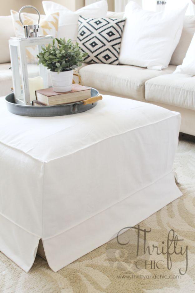 White ottoman slipcover with kick pleated corners in front of a white sofa, topped with a tray and a small plant