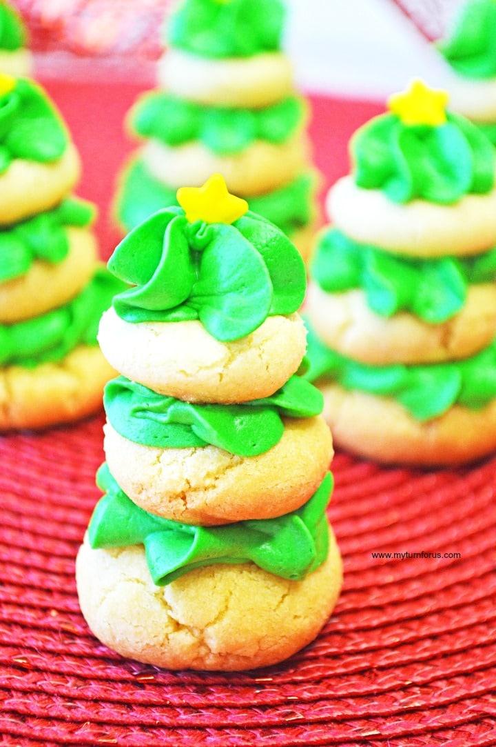 Three tiered sugar cookie Christmas trees with piped green cream cheese frosting and yellow star sprinkles on a red woven mat