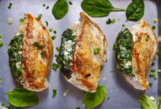 Spinach stuffed chicken breasts on a metal tray, creamy spinach and feta filling sitting in the open pocket of each