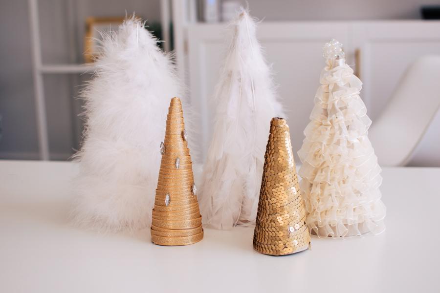 Five cone trees covered in white feather boa, gold glitter ribbon, gold sequins and ruffled cream ribbon on a white desk