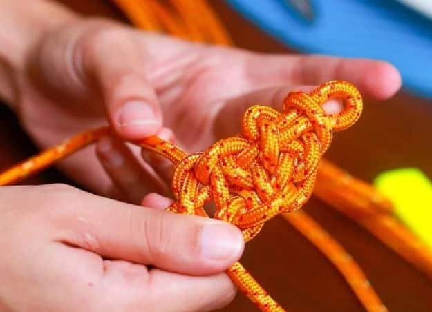 Hands weaving a bright orange blaze bar paracord bracelet in progress, showing the flat bar weave forming