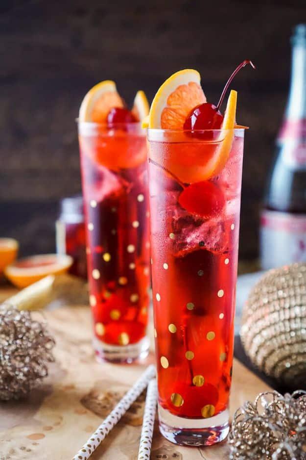 Two tall glasses of champagne Shirley Temple with crushed ice, maraschino cherries and orange slice garnishes