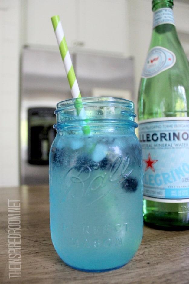 Blue mason jar of sparkling water with blueberries and a striped straw beside a green Pellegrino bottle