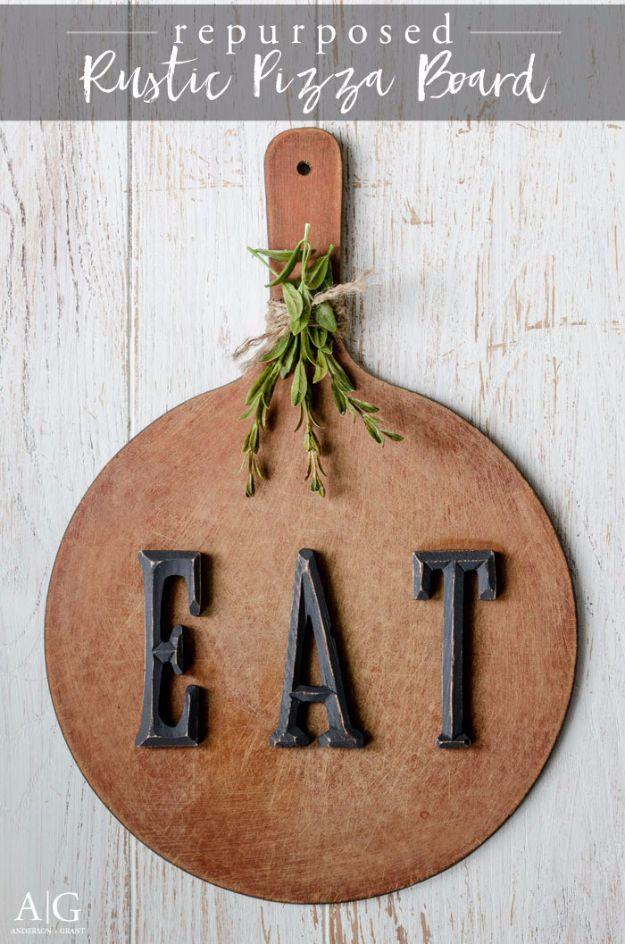 A wooden pizza peel lettered in black hangs flat on a kitchen wall, its paddle aged to a soft gray farmhouse finish