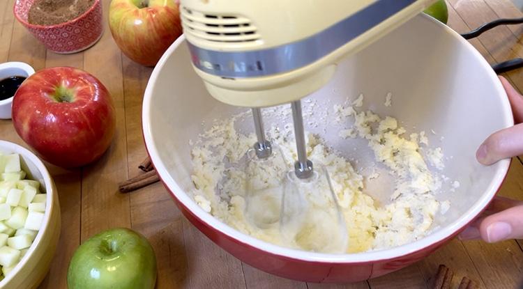 Breakfast Recipes - yellow hand mixer beating butter and sugar in a red bowl while one hand steadies it, with apples and a bowl of diced apple nearby