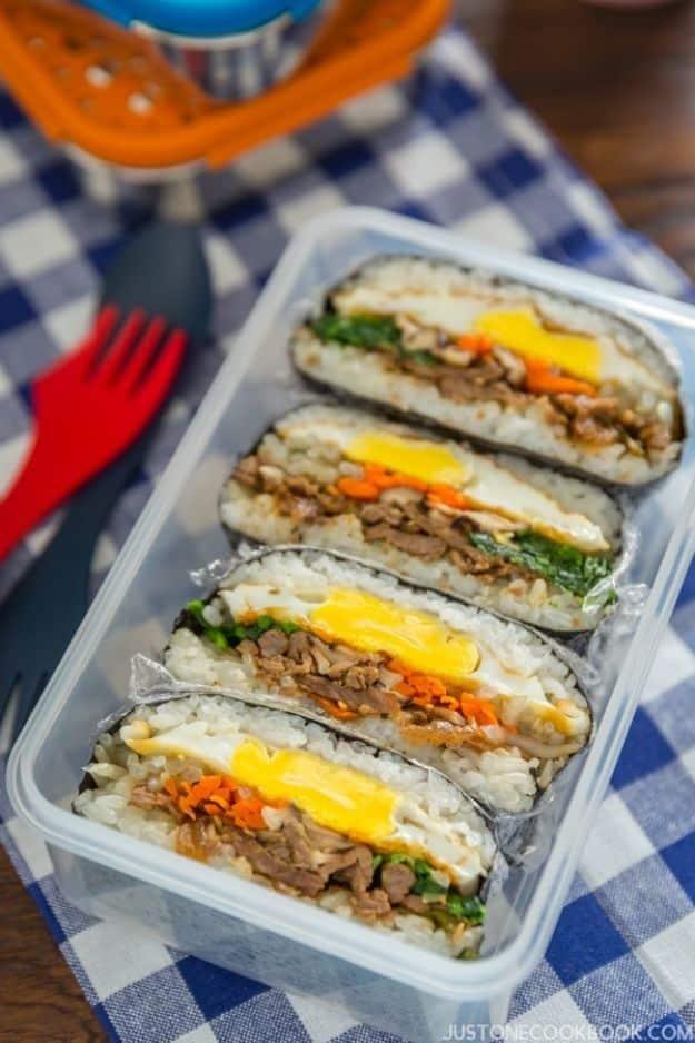 Bulgogi onigirazu rice sandwiches cut in half in a lunch box showing beef, egg and vegetables in nori