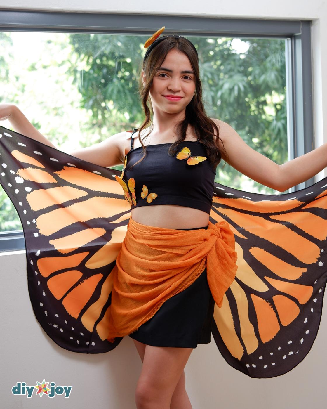 No-Sew Halloween Costume - woman by a window with both wings spread wide, wearing a butterfly headband and orange sarong