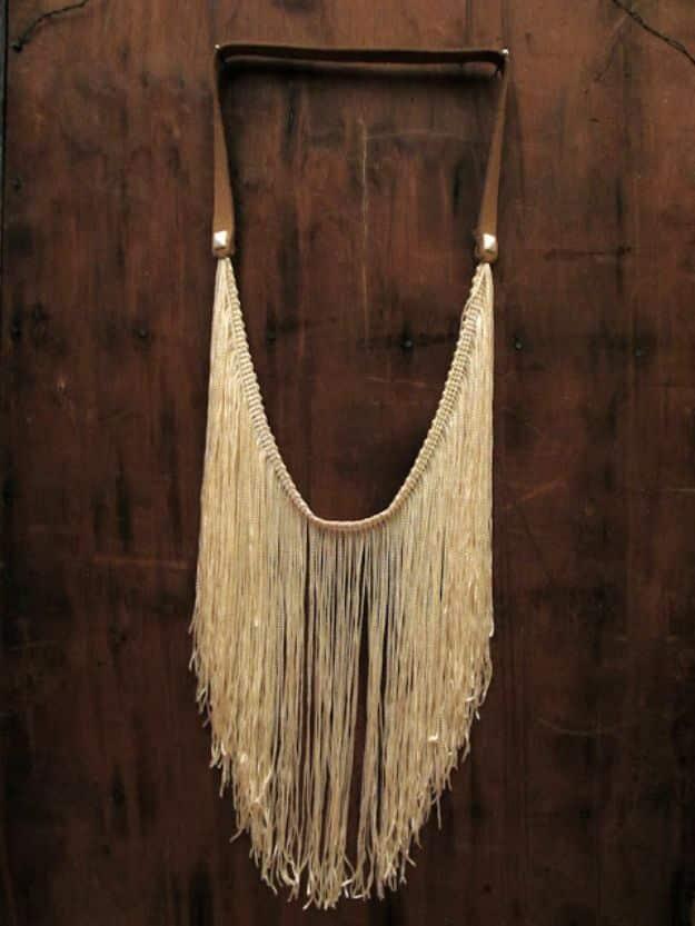 Pale chainette fringe necklace hanging from a studded dark leather strap, displayed on a wooden board
