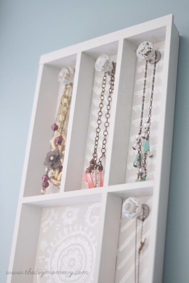 Wall mounted wooden cutlery tray painted grey and white, holding necklaces and bracelets on glass knobs and hooks