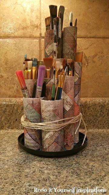 Cardboard tubes covered in patterned paper on a plastic lid, holding paint brushes sorted short at front, tall behind
