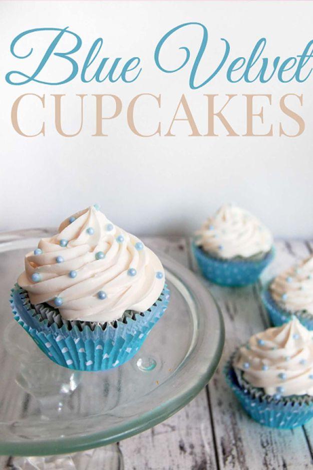 Blue velvet cupcakes in blue liners with white buttercream swirls and blue pearls on a glass cake stand