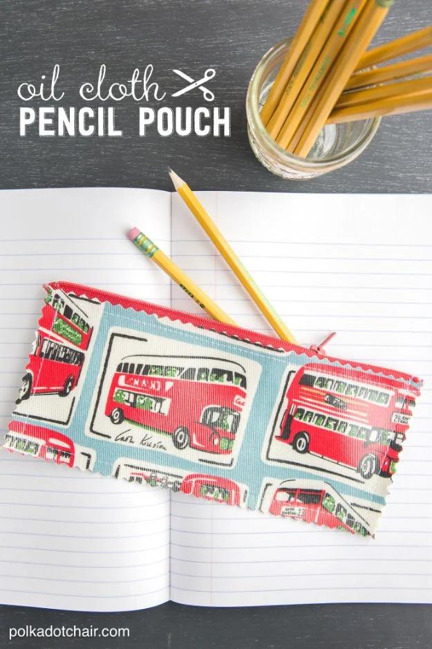 Oilcloth pencil pouch graphic, a red double decker bus print zip pouch on an open lined notebook with yellow pencils in a jar