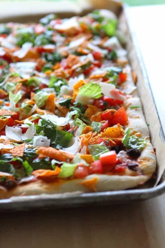 Taco salad pizza topped with shredded lettuce, roma tomatoes, black beans, cilantro and crushed Doritos