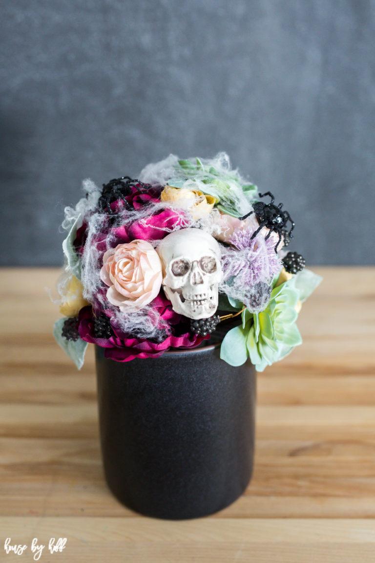 Colorful fall bouquet in a black crock with one white skull, faux cobweb and black jeweled spiders, plus House by Hoff mark