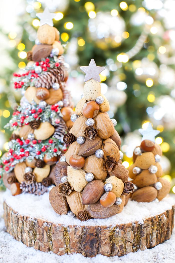 Three tabletop trees covered in whole nuts, mini pinecones and silver glitter berries with star toppers on a wood slice