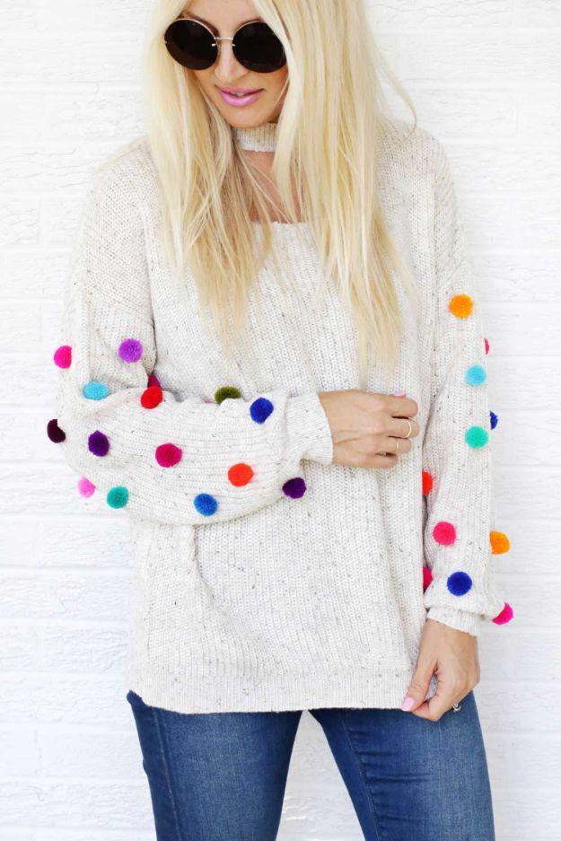 Cream knit sweater with bright multicolored pom poms sewn all over both sleeves, worn with blue jeans