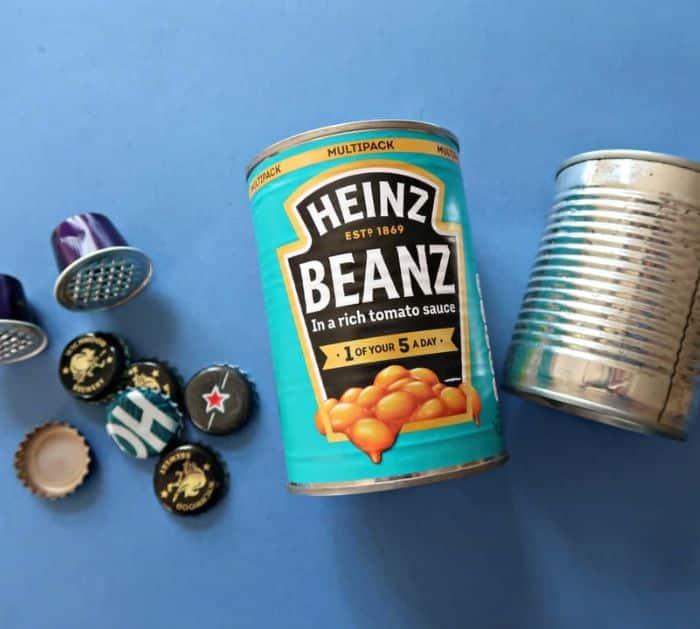 Sueeye pin graphic, DIY Tin Can Owl, a finished tin can owl with bottle cap eyes and a dark beak, in a hedge