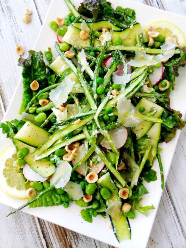 Spring salad on a white platter with asparagus, zucchini ribbons, peas, radishes, hazelnuts and shaved cheese