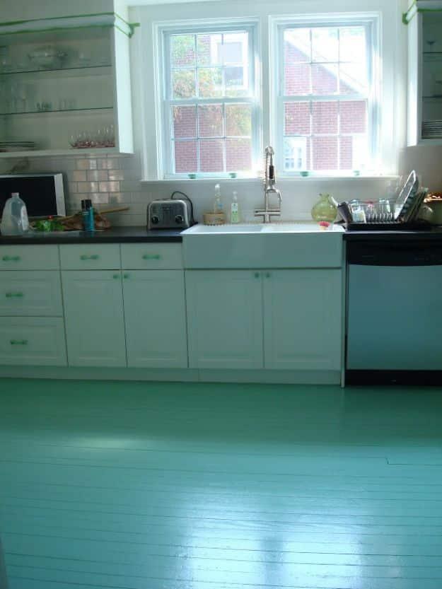 DIY painted kitchen floor, glossy sea green painted floorboards under pale mint cabinets and a farmhouse sink