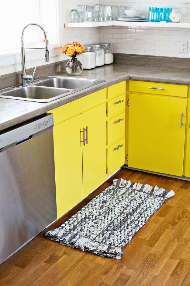 Grey and white woven rag DIY rug with short fringed ends on wood floor in a kitchen with bright yellow cabinets