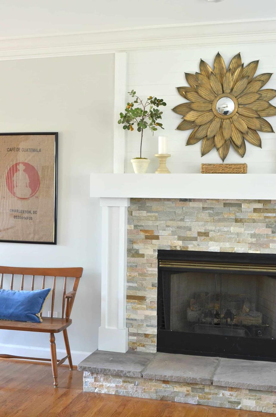 Fireplace faced in stacked stone tile with a white painted mantel and a gold sunburst mirror hanging above it