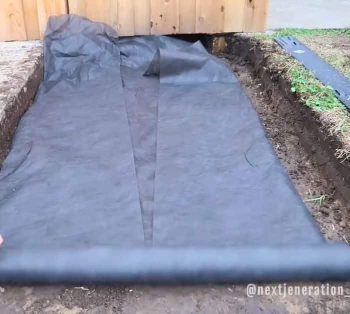 Trench for a drainage pathway lined with black weed barrier fabric before the limestone base goes in