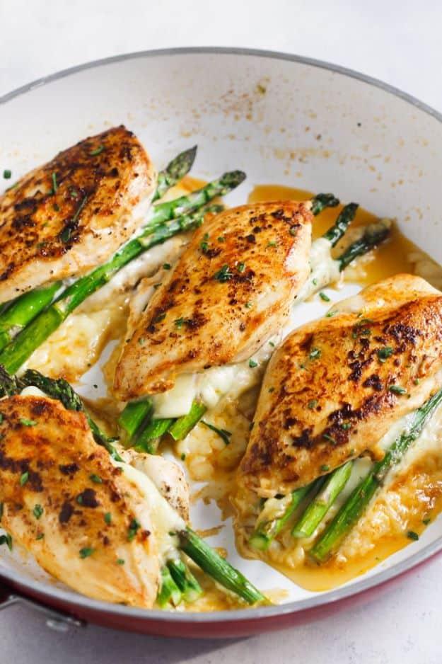 Asparagus stuffed chicken breast in a skillet, four browned chicken pieces with asparagus spears and sauce