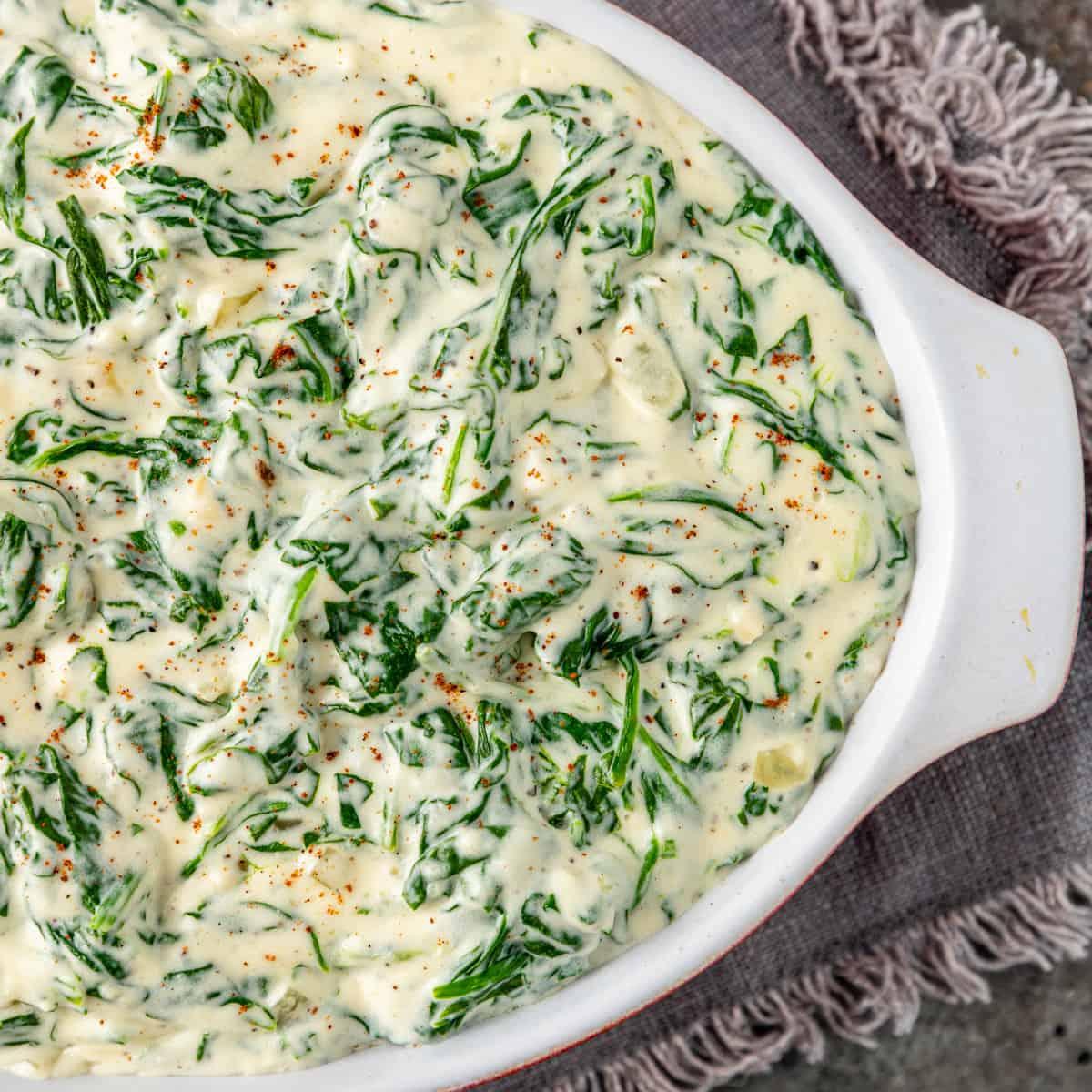 Creamy steakhouse creamed spinach in a white oval baking dish resting on a grey fringed linen napkin