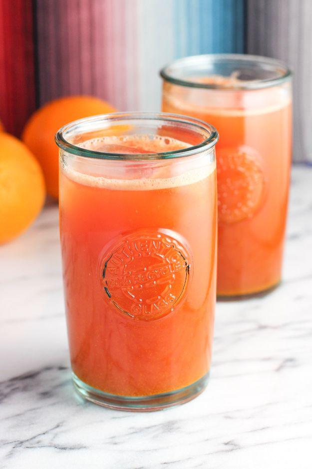 Watermelon orange ginger turmeric juice in two heavy glasses on marble with whole oranges just behind