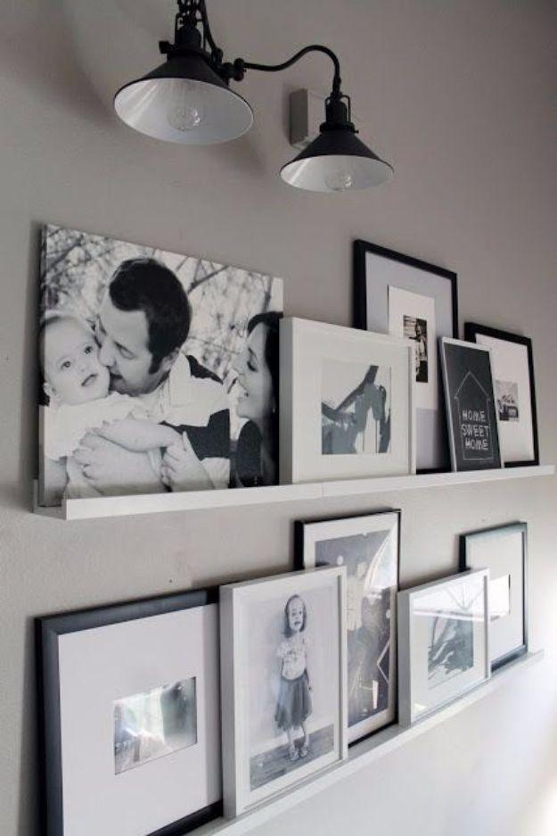 Two long white picture ledges on a grey wall holding a large leaning black and white canvas and overlapping framed prints