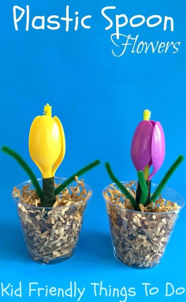 Two crocuses of purple and yellow plastic spoons on green wrapped stems with pipe cleaner leaves, in cups of shavings