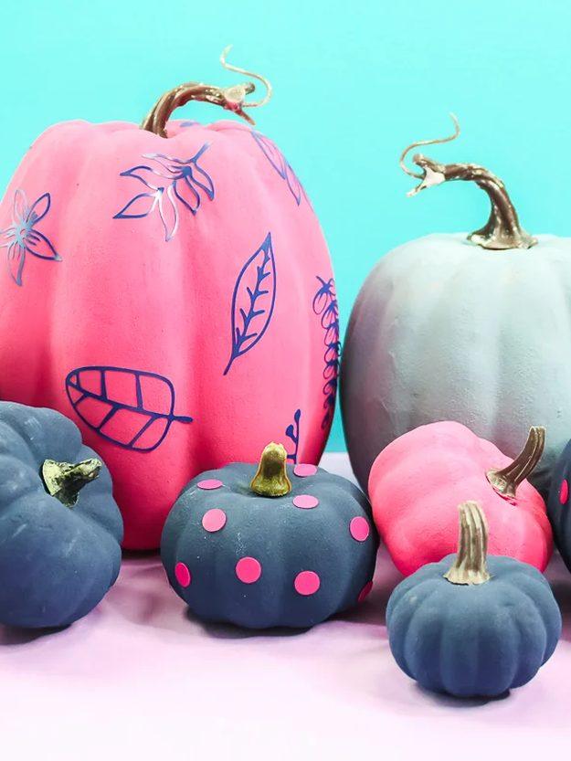 Pink, navy and gray painted craft pumpkins decorated with cut vinyl leaves and rows of hot pink polka dots