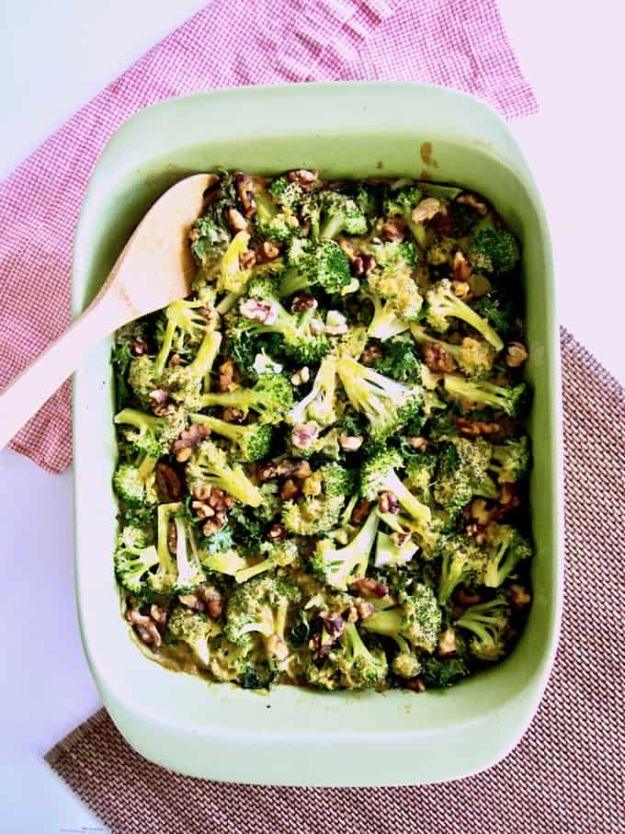 Broccoli kale and rice casserole in a mint green baking dish topped with chopped nuts with a wooden spoon in it