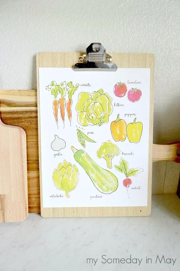 Watercolor vegetables printable clipped to a wooden clipboard on a marble counter, a free printable craft idea