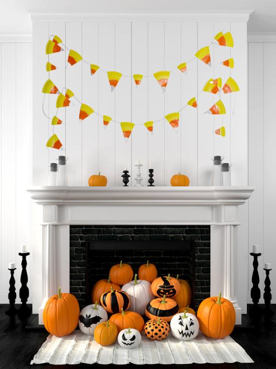 A paper plate candy corn banner in orange, yellow and white strung in two swags across a white mantel above pumpkins