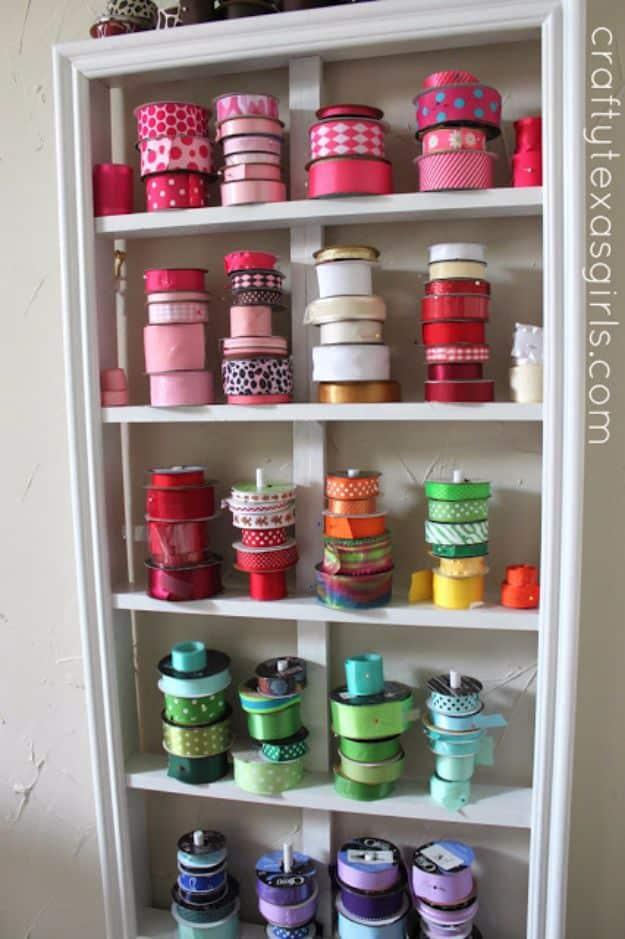 White five shelf bookcase with rods across each shelf holding ribbon spools grouped by color from pink through purple