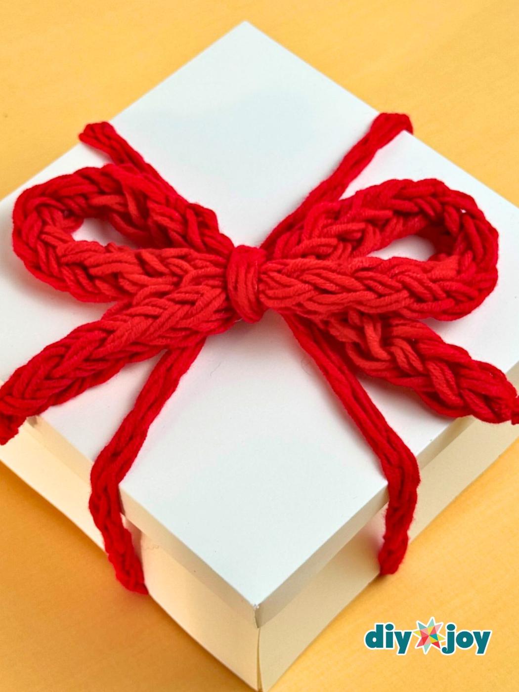 A soft bow finger crocheted from leftover cream yarn, sitting on a wrapped parcel as a no hook topper