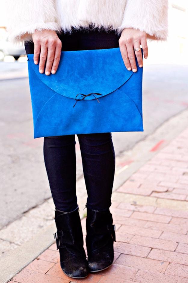 Cobalt blue suede envelope clutch with a curved flap and a dark ribbon tie held against a white fur coat