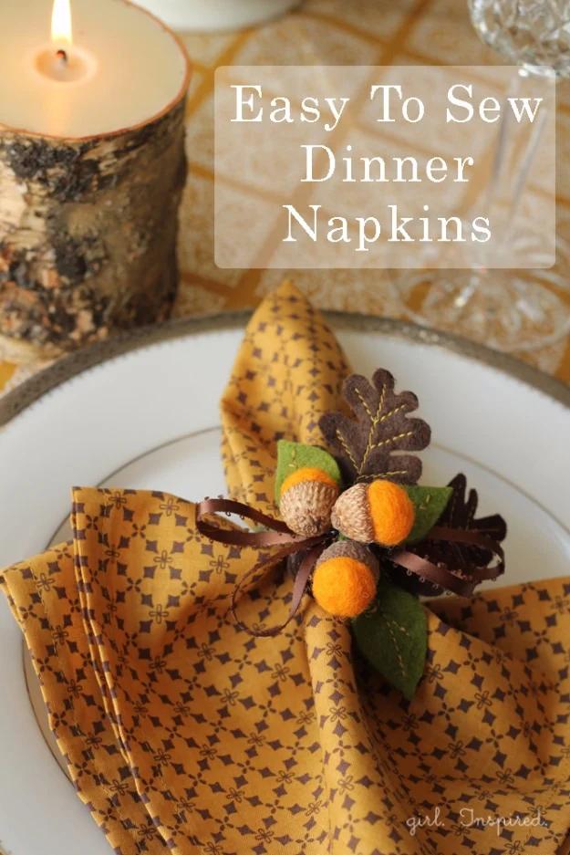 Gold print dinner napkin folded on a white plate with an acorn napkin ring, candles lit in the background