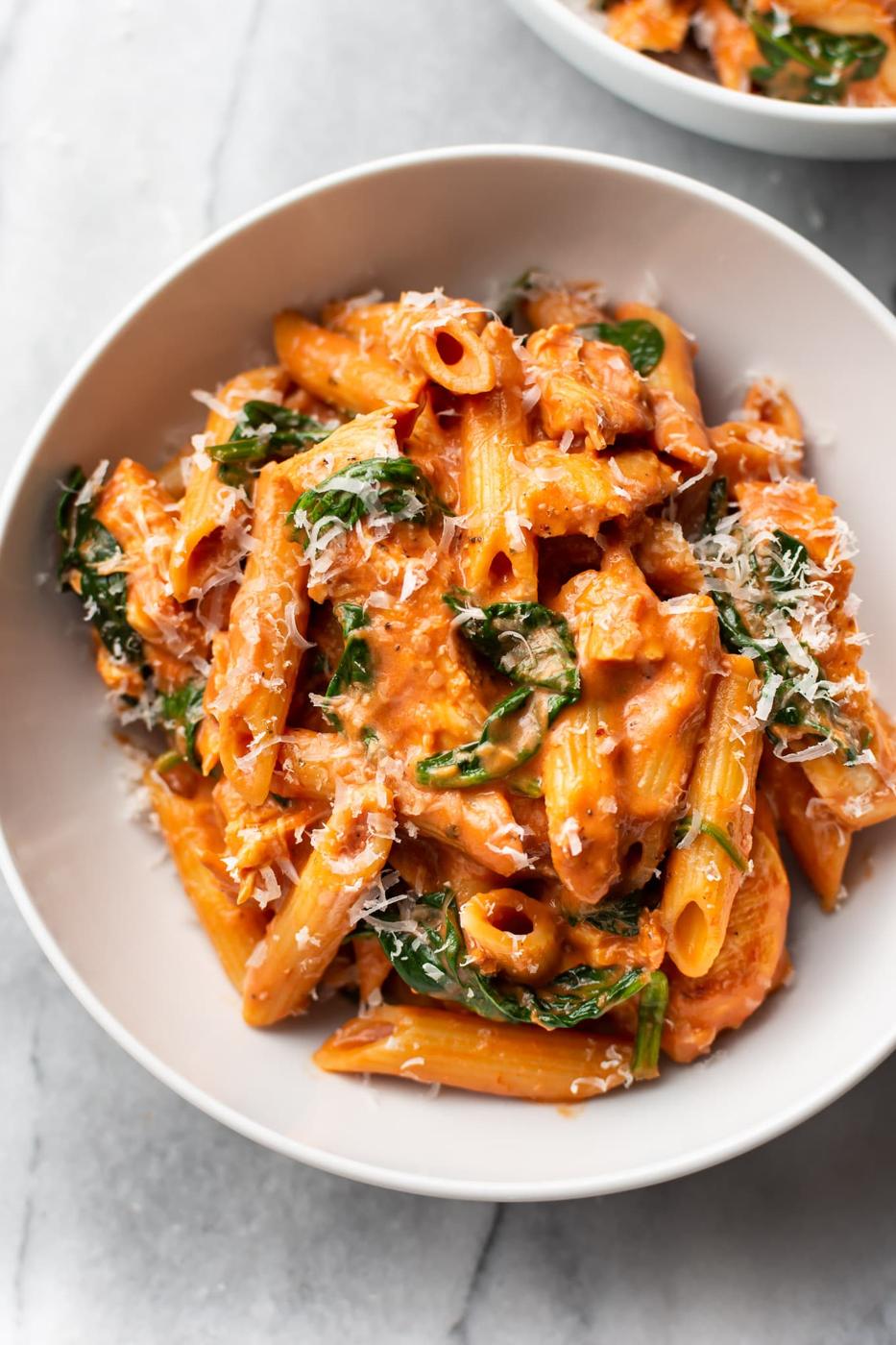 Tomato spinach chicken pasta with penne in a creamy tomato sauce and grated parmesan in a white bowl