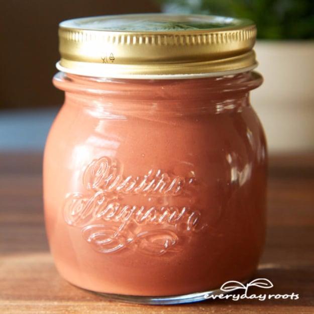 Homemade calamine lotion, terracotta pink lotion in a clear embossed glass jar with a gold lid on wood