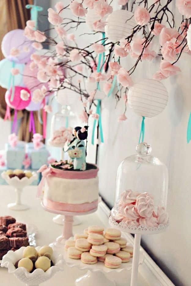 Bare branches covered in pale pink tissue paper blossoms with hanging paper lanterns above a pink dessert table