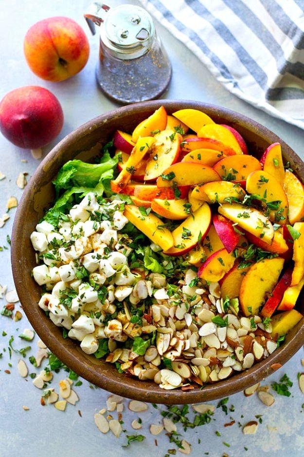 Peach salad in a wooden bowl with sliced peaches, greens, crumbled cheese and toasted chopped nuts on top